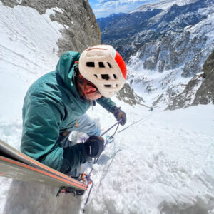 Ski Guide, Eric Shaw, belays a skier up a snow-filled couloir.